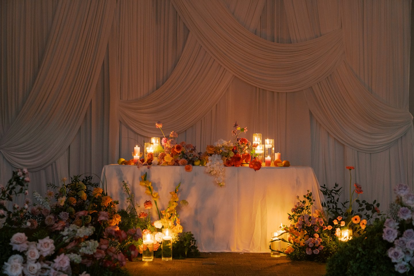 Hochzeitstisch mit orangefarbenen Blumenarrangements und Kerzenlicht.